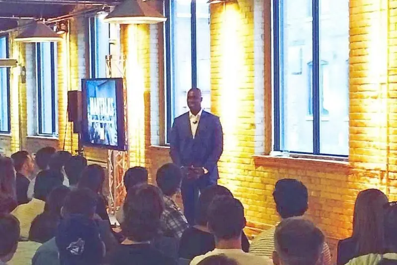 Gary Durrant speaking to a seated audience in a brick-walled hall